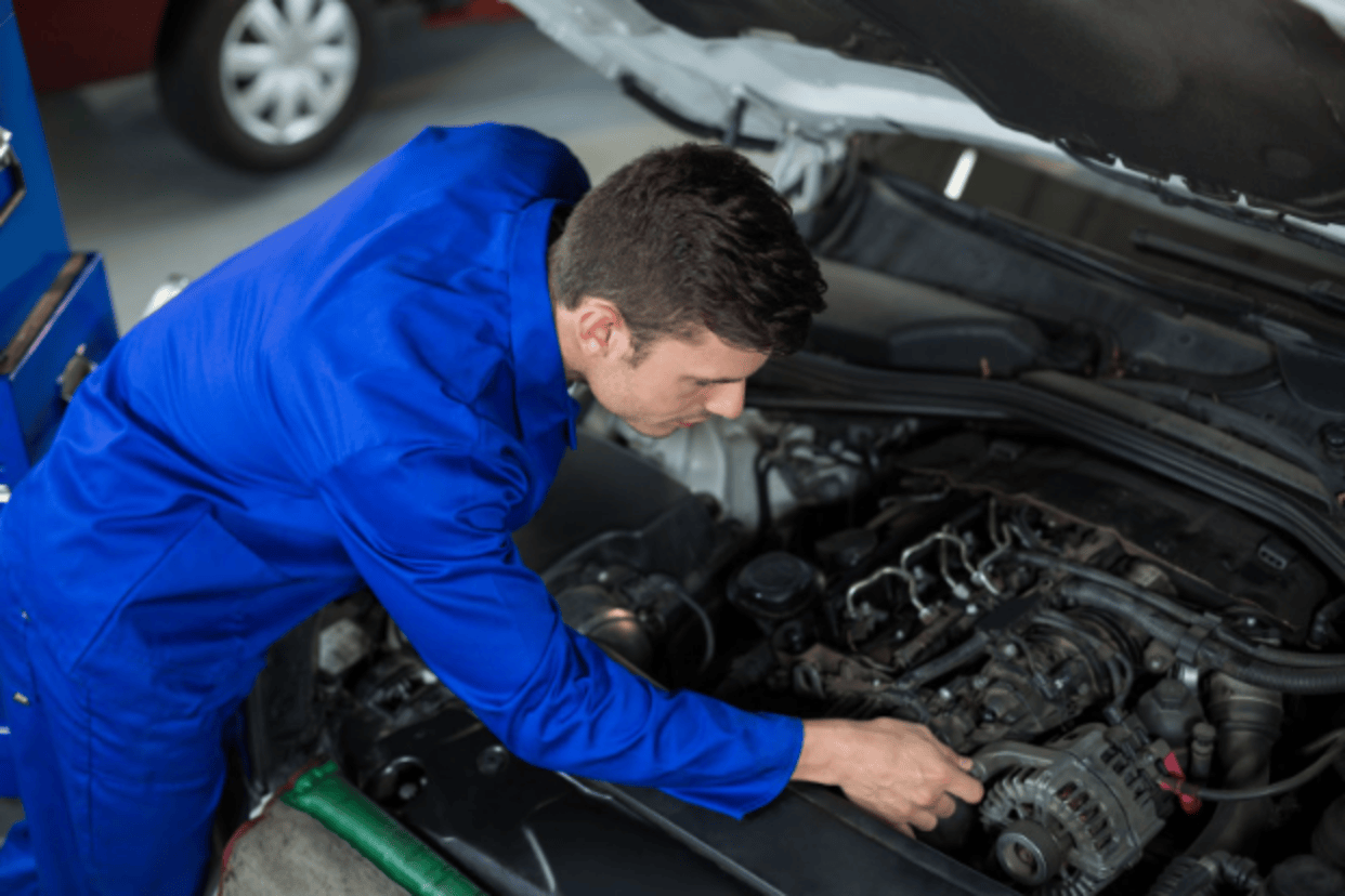 Mechanic inspecting a car engine under the hood in an auto repair shop.